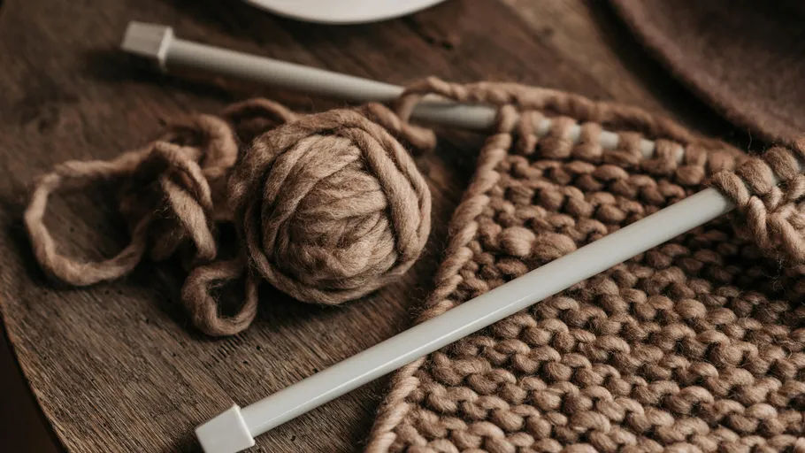 Stricknadeln mit brauner Wolle auf Tisch.