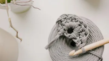 Gray yarn being crocheted with wooden hook.