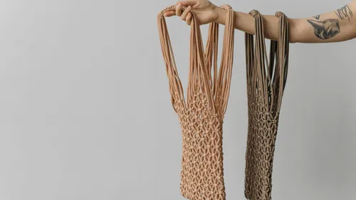 Hand holding two macrame bags sideways.