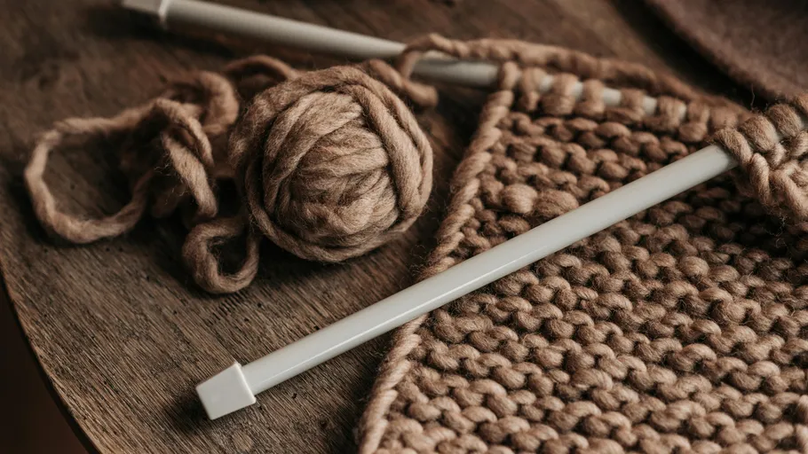 Stricknadeln mit brauner Wolle auf Tisch.