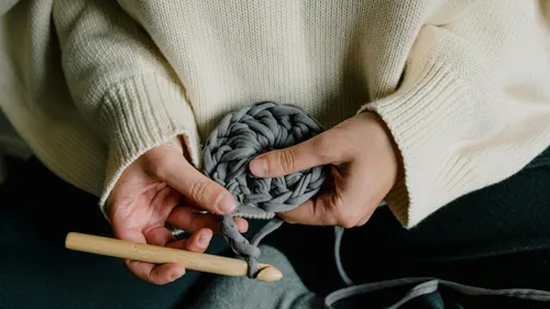 Hands crocheting with grey yarn indoors.