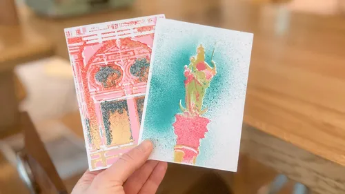 Hand hält zwei bunte Postkarten im Innenraum.