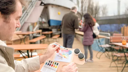 Person painting at outdoor cafe with tables.