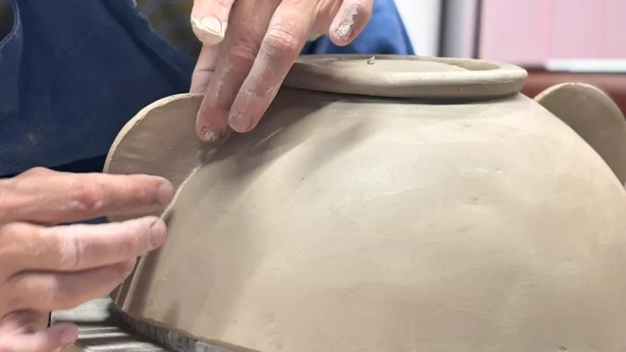 Hands molding clay on pottery wheel.