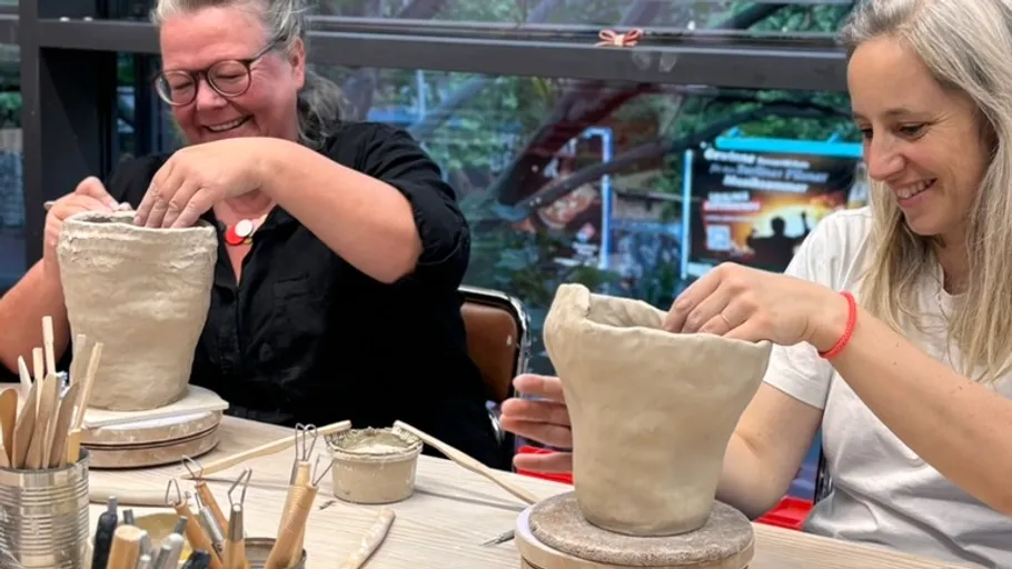 Two women crafting clay pots indoors.
