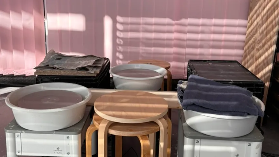 Zwei Becken mit Wasser auf Kisten, von Stühlen umgeben.