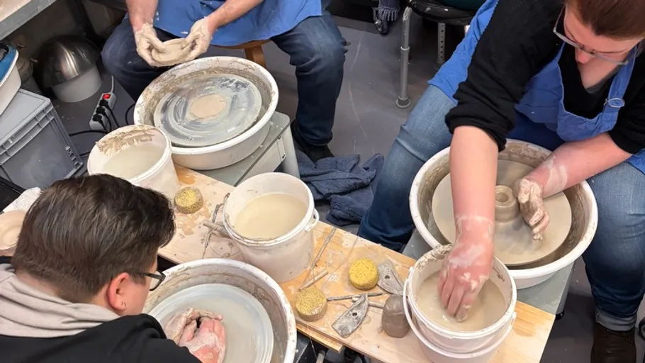 People crafting pottery on wheels in studio.