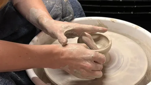 Hands shaping clay on pottery wheel.