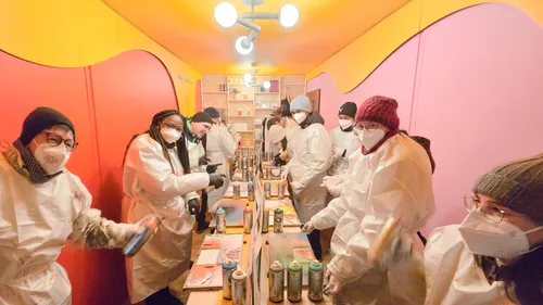 People in protective gear spray paint in workshop.