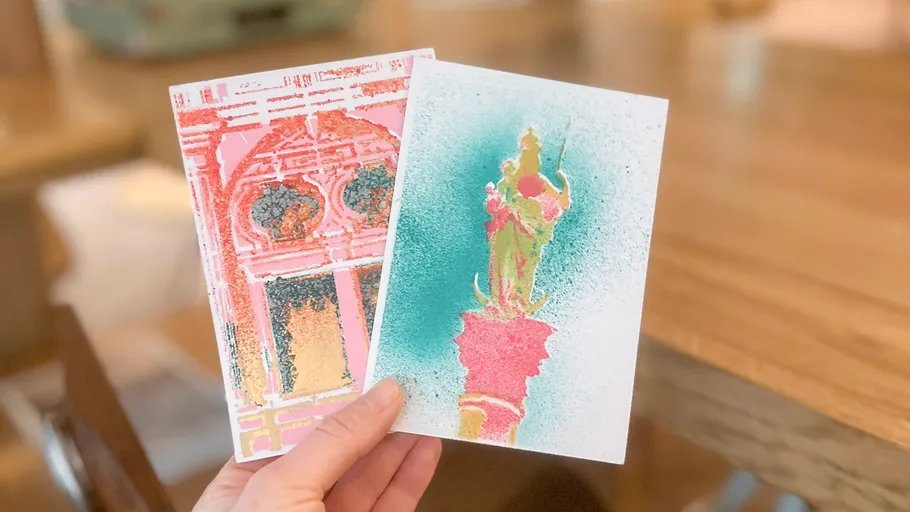 Hand holding two artistic postcards on table.