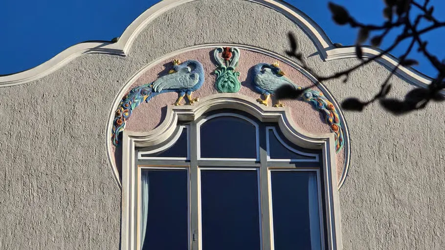 Dekorative Vögel über Bogenfenster, verzierte Fassade.
