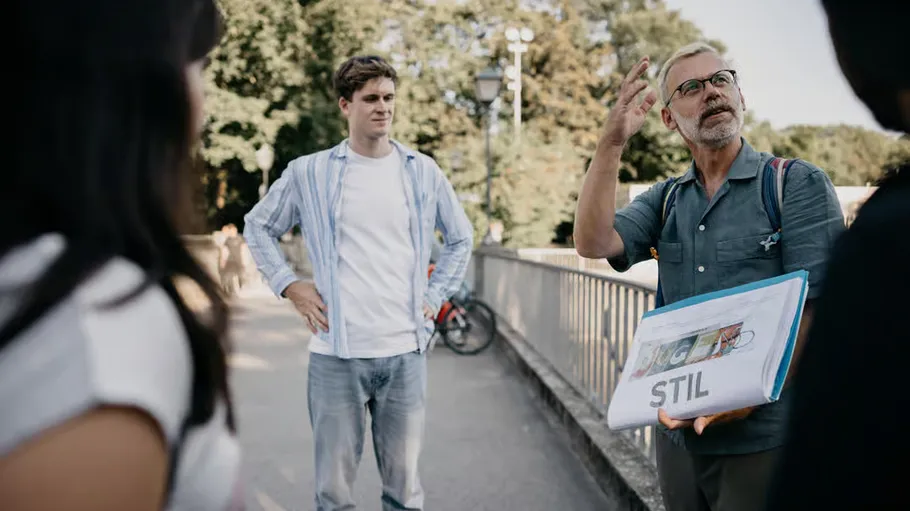 Man holding sign, talking outdoors to small group.