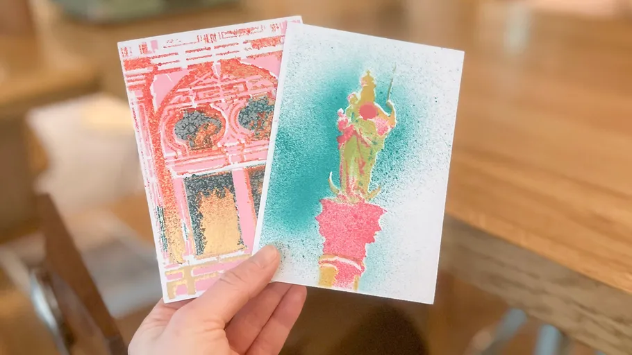 Hand holding two colorful art cards indoors.