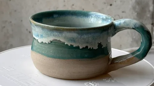 Ceramic mug with green-blue glaze on table.