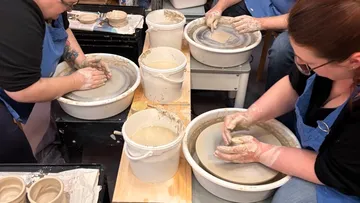 People molding clay on pottery wheels indoors.