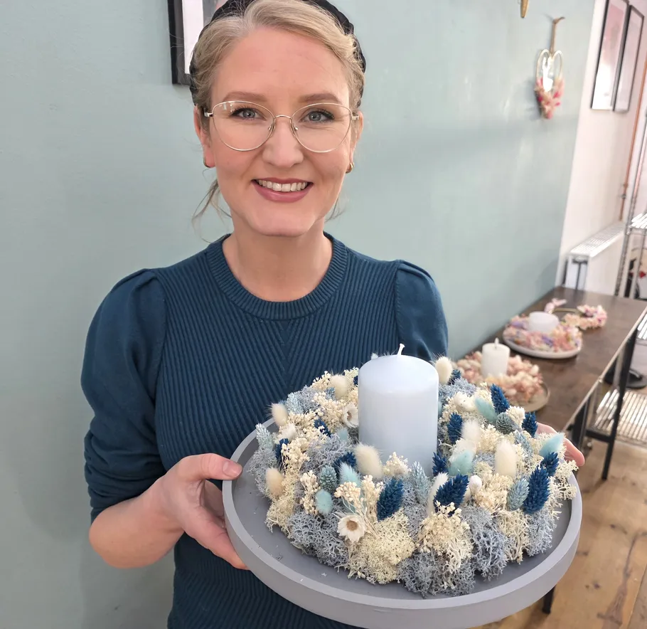Woman holding decorated candle arrangement indoors.