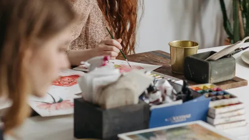 Person malt an einem Tisch mit Kunstbedarf.