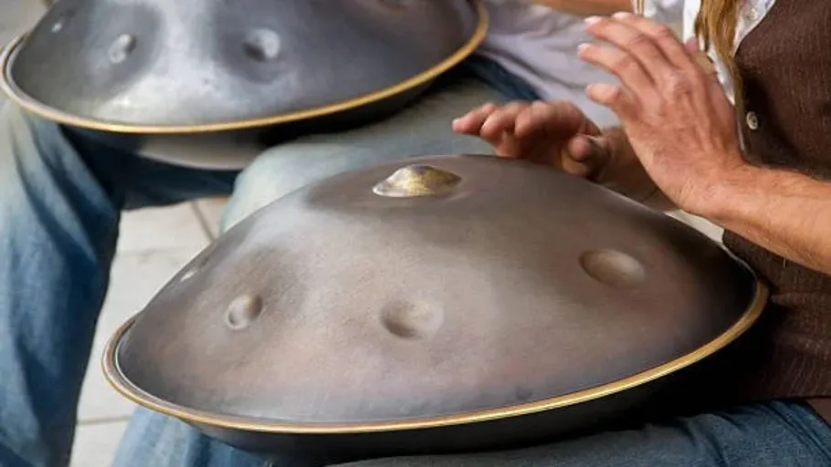 Hands playing a hang drum on laps.