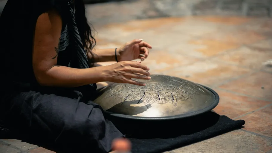Person playing handpan on floor outdoors.