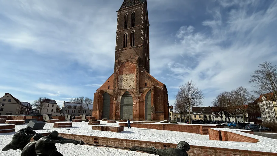 Hoher Backsteinkirchturm auf verschneitem Platz.