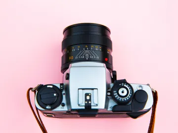 A camera is lying on a pink background.