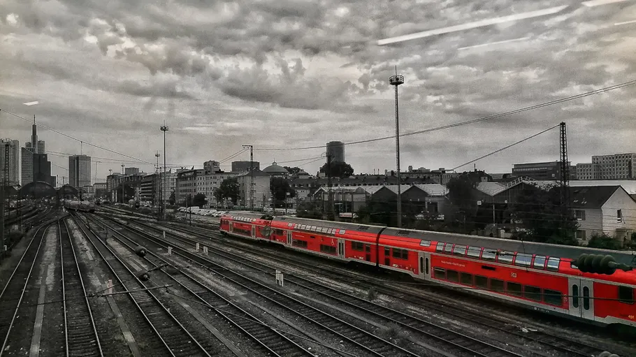 Red train on tracks under cloudy sky.