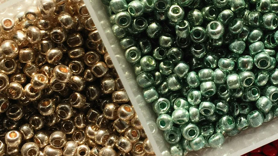 Goldene und grüne Perlen in Plastikbehältern.
