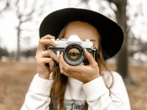 Woman holding camera, looking in, surrounded by trees.