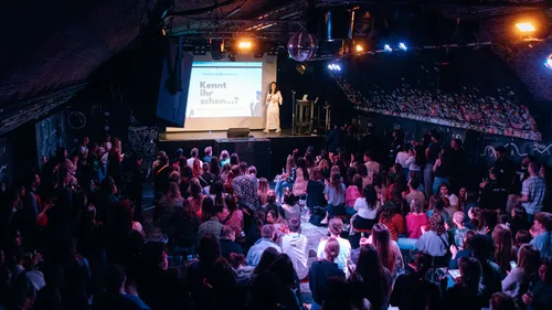Woman speaking to crowd in a dimly lit venue.