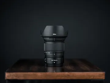 Camera lens stands on a wooden background against a black background.