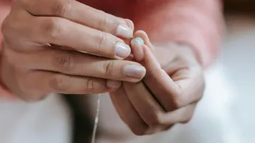 Hands threading a needle in indoor setting.