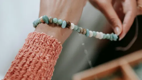 Hände fädeln Perlen auf einem Armbandfaden.