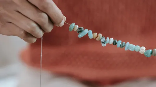 Hand threading multicolored beads on string.