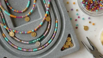 Colorful beaded necklaces with gold coins on tray.
