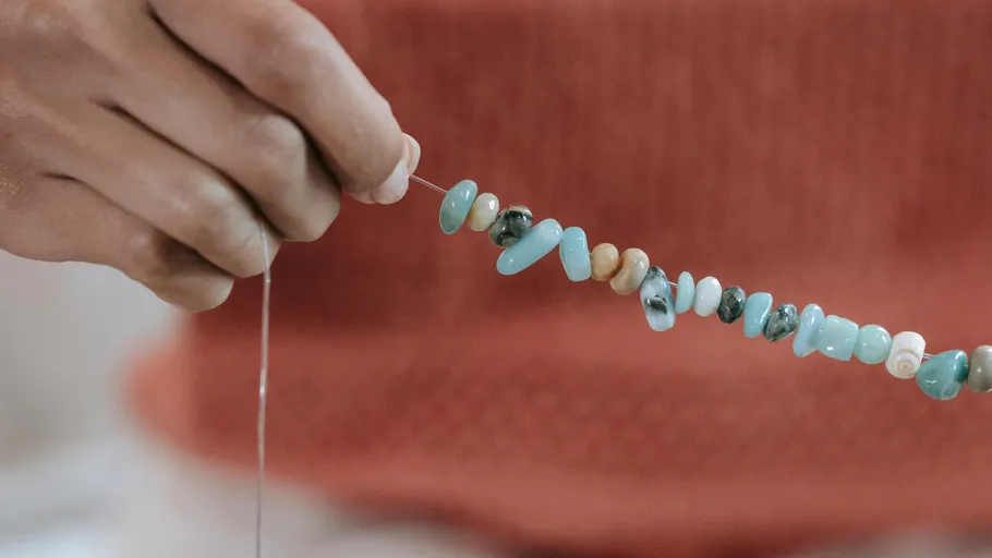 Hand threading beads on a string, indoor setting.