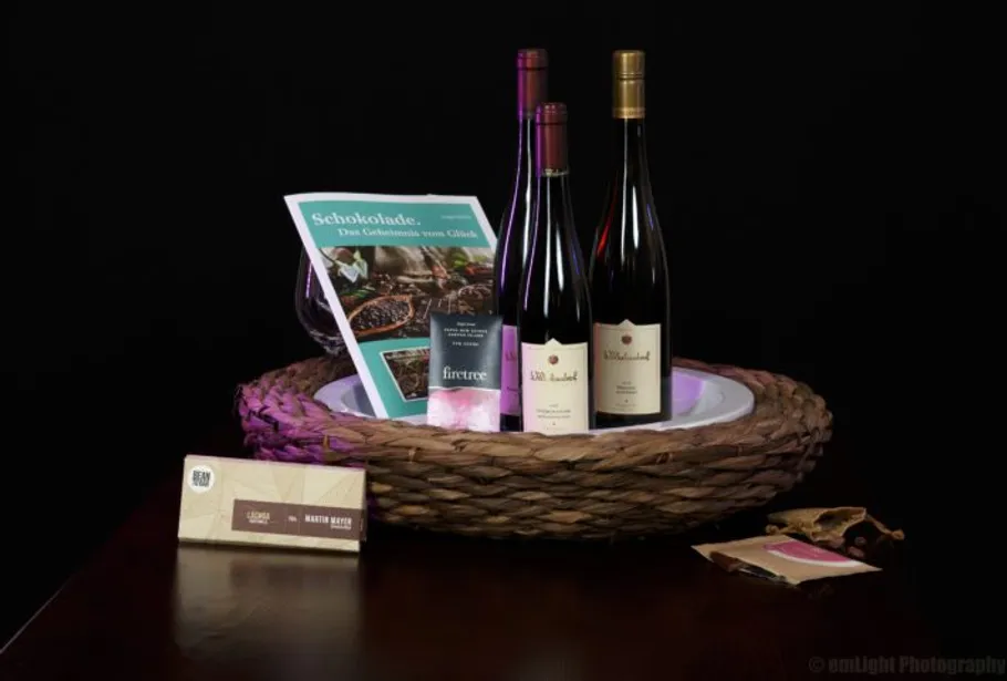 Wine bottles are in a basket with chocolate and a brochure.