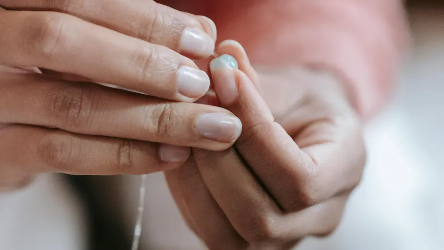 Hands threading blue bead with string.