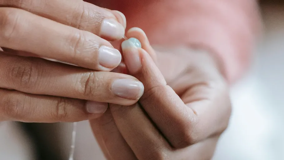 Hands threading a small blue bead.