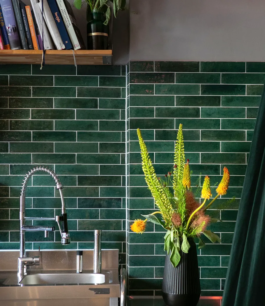 Kitchen sink with flowers on dark green tiles.