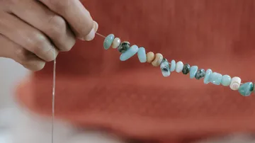 Hand hält einen Faden mit bunten Perlen.