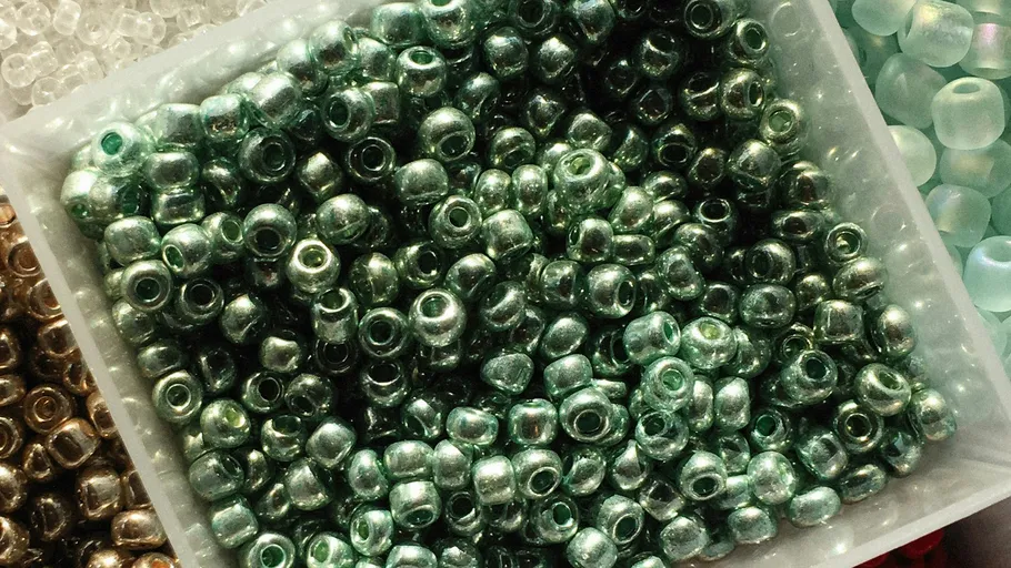 Green beads in a container, surrounded by other beads.