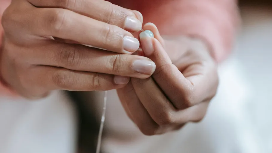 Hands threading a blue bead onto string.