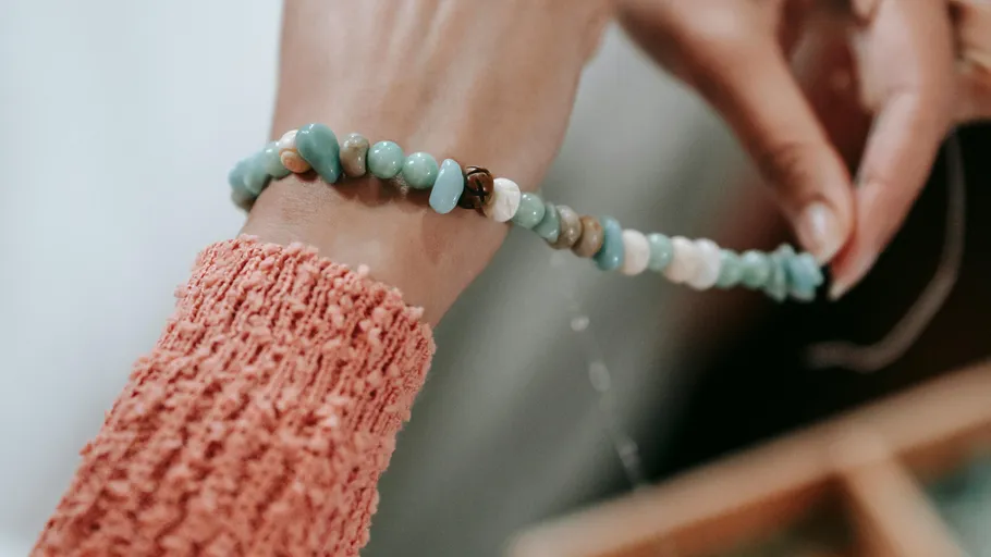 Person making beaded bracelet on wrist.