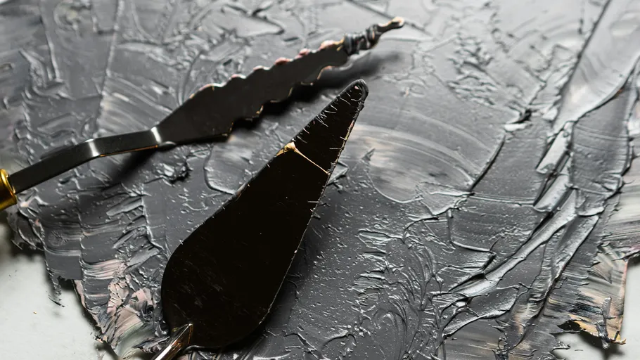 Palette knives with black paint spread on surface.