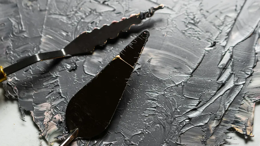 Palette knives spreading thick gray paint.