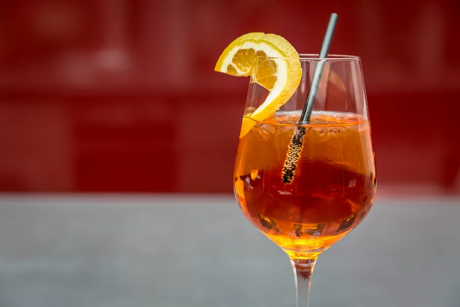 Orangener Cocktail mit Zitronenscheibe, roter Hintergrund.