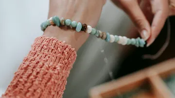 Person fädelt türkise Perlen auf Armband.