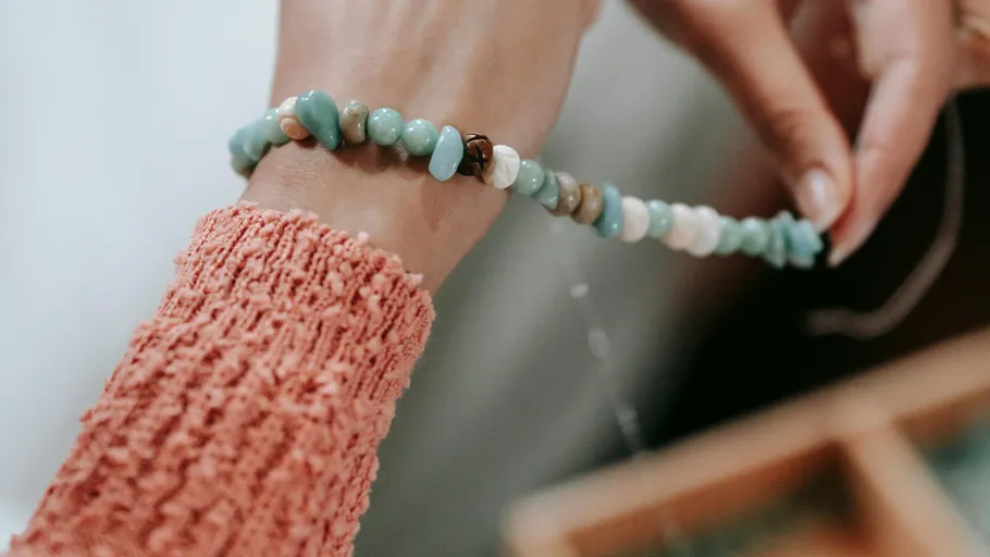 Person stringing turquoise beads on bracelet.