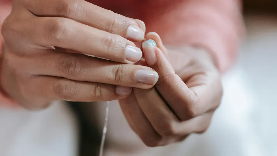 Hands threading a blue bead indoors.