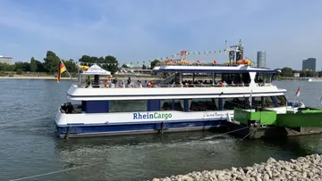 Ferry boat decorated with flags docked at riverbank.